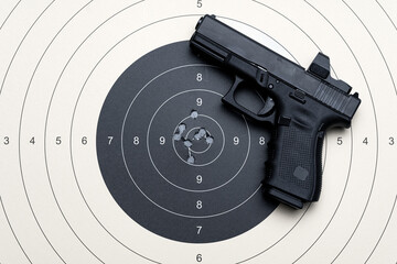 A target for shooting with bullet holes in the center and a pistol with a red dot sight.