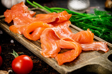 Slices of salted salmon on a cutting board with dill and tomatoes.