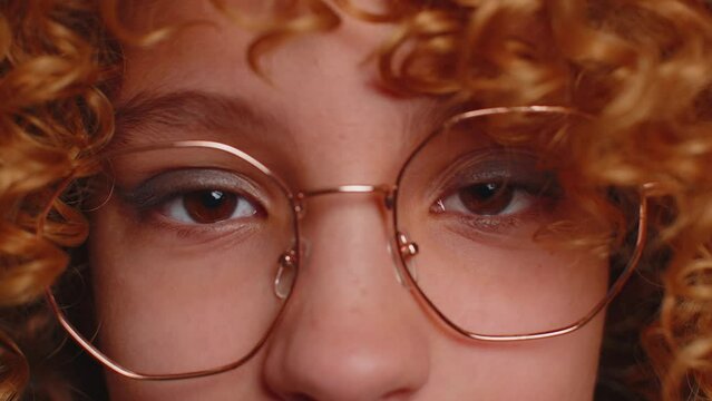 Extreme close-up macro portrait of smiling girl face. Teen beautiful kid's eyes, looking at camera. Brown eyes of redhead female child model. Young children in eyeglasses opening wide her closed eyes