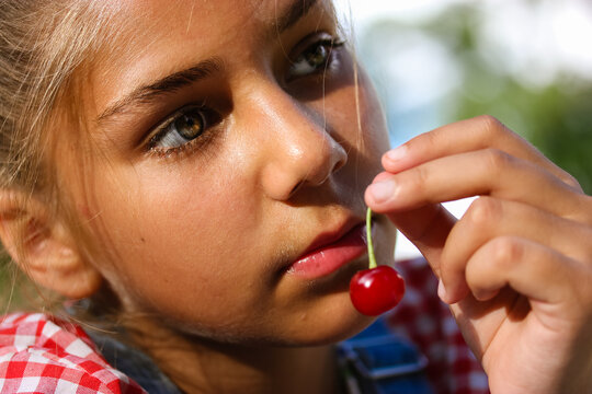 A little teenage girl holding a ripe red cherry in the fruit trees orchard. Portrait of a beautiful oriental tanned child, female kid 10-12 years old in summer nature. Natural hippie children beauty.