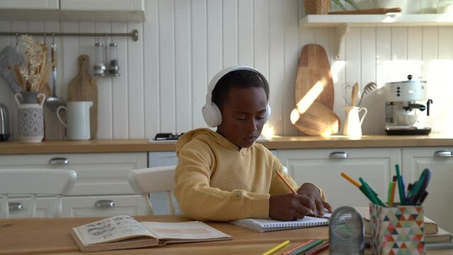 Focused kid African American boy sitting at desk working on engineering project, child using drafting tools ruler and pencil doing geometry homework, while studying at home. Technical drawing for kids