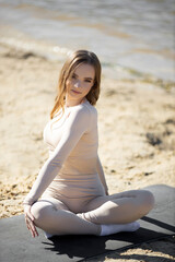 Fototapeta na wymiar beautiful young woman with a slim figure is doing yoga near the sea