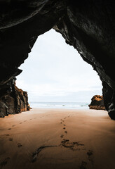 photo of footprints in cave with ocean on background in sunrise. Low tide in seaside cave with golden sand on the beach with rocks on background. Beautiful and peaceful cave with view on blue ocean.