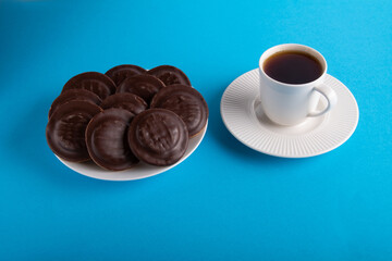 photo on a plate with chocolate chip cookies next to a cup with a drink on a saucer