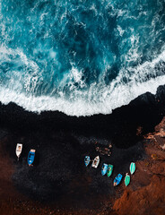 Vertical aerial photo of black sand volcanic beach with boats on the shore and big and strong waves...
