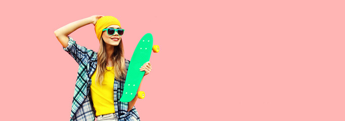 Summer portrait of happy smiling young woman with skateboard wearing colorful clothes looking away on pink background, blank copy space for advertising text