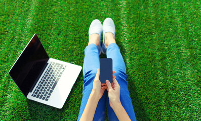 Woman working with laptop and smartphone in the park on green grass background, top view