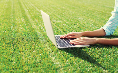 Female hands woman working with laptop in the park on green grass background