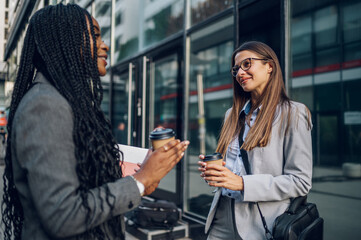 Two multiracial business woman meeting outside and drinking coffee