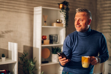 Fototapeta na wymiar Middle aged man using smartphone and drinking coffee at home