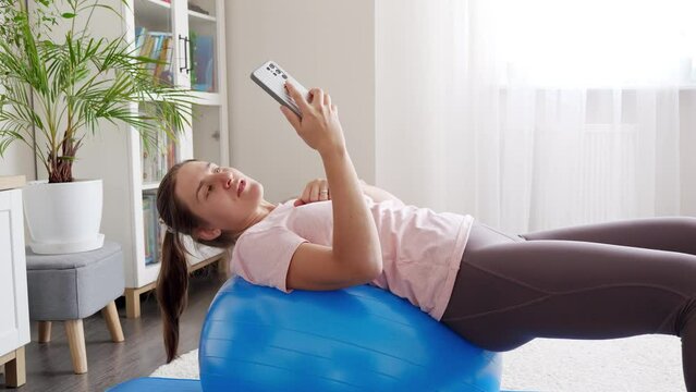 Young woman shooting video on smartphone of her fitness training and sports exercises on fitball. Sports, fitness and yoga bloggers and influencers.