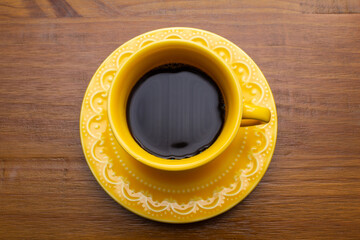 Uma xícara amarela de café preto com um pires amarelo sobre uma mesa de madeira.