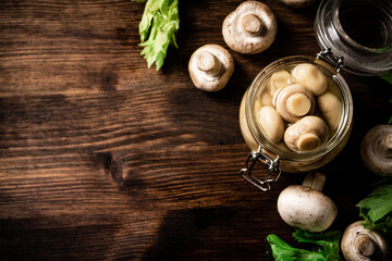 A small glass jar with pickled mushrooms on the table. 
