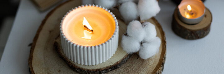 Cozy autumn or winter composition with aromatic candle, wool sweater, cotton, book. Aromatherapy, home atmosphere of cosiness and relax. Wooden background close up. Banner