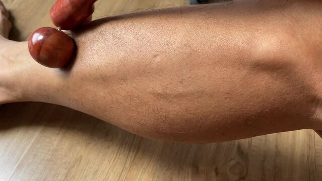 Male hand pressuring Thai traditional roller ball wooden massage stick on leg muscle. Health body and skin concept