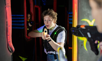 Fototapeta na wymiar Emotional young man with laser pistol playing laser tag with friends on dark labyrinth