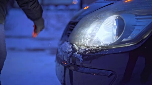 Cleans car headlight with plastic shovel from ice and snow.