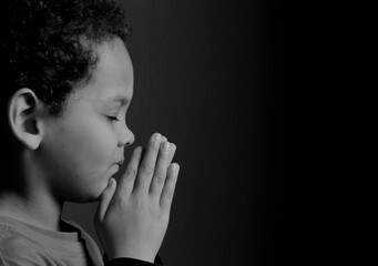 child praying to God with hands together with black background with people stock photo 