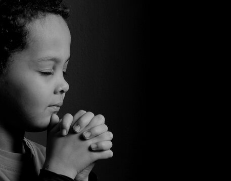 child praying to God with hands together with black background with people stock photo 