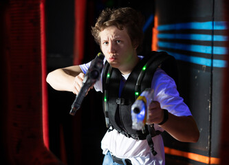 Emotional young man with laser pistol playing laser tag with friends on dark labyrinth