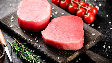 Fresh raw tuna on a cutting board with tomatoes, spices and rosemary. 