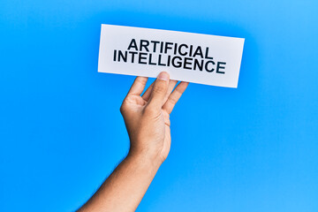 Hand of caucasian man holding paper with artificial intelligence message over isolated blue background