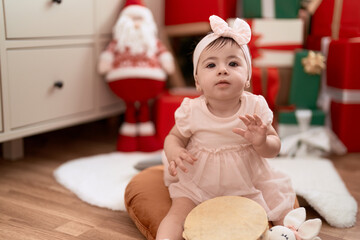 Adorable toddler playing tambourine sitting on floor by christmas gift at home