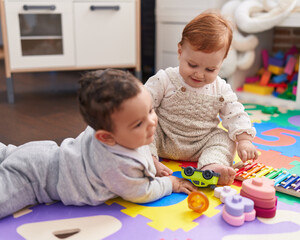 Obraz premium Two adorable babies playing with toys sitting on floor at kindergarten