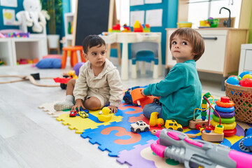 Two kids playing with cars toy sitting on floor at kindergarten