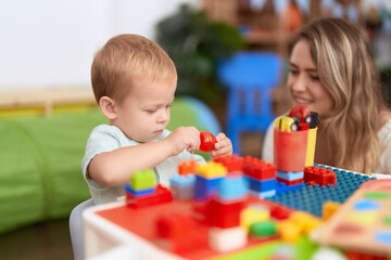 Teacher and toddler playing with construction blocks sitting on table at kindergarten