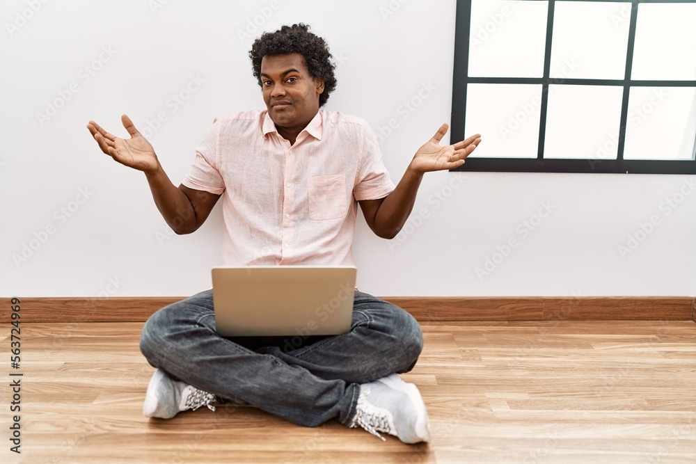 Canvas Prints african man with curly hair using laptop sitting on the floor clueless and confused expression with 