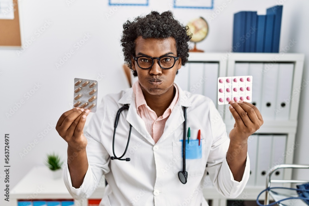 Canvas Prints african man wearing doctor uniform holding prescription pills puffing cheeks with funny face. mouth 