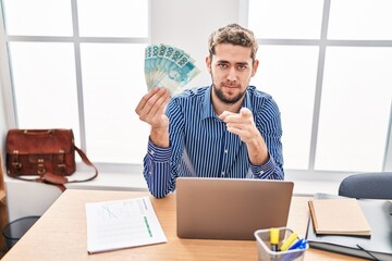 Hispanic man with beard working at the office holding brazilian reals pointing with finger to the camera and to you, confident gesture looking serious