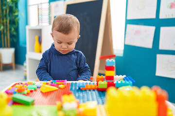 Adorable blond toddler playing with construction blocks standing at kindergarten