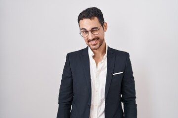 Handsome business hispanic man standing over white background winking looking at the camera with sexy expression, cheerful and happy face.
