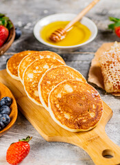 Homemade pancakes on a cutting board with honey and berries. 