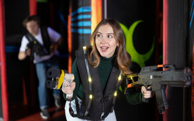 Positive girl holding laser pistol playing laser tag game with his friends