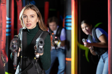 Smiling girl with laser pistol during playing laser tag with her friends in dark room