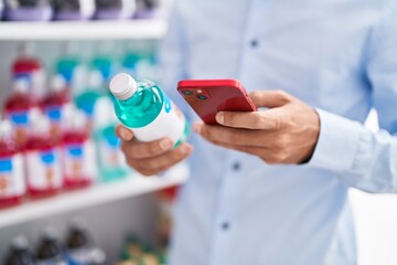 Young hispanic man customer using smartphone holding medicine bottle at pharmacy