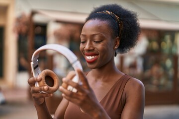 African american woman smiling confident holding headphones at street