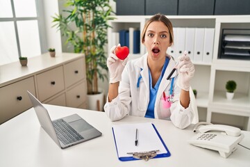 Young blonde woman wearing doctor uniform holding blood and heart afraid and shocked with surprise...