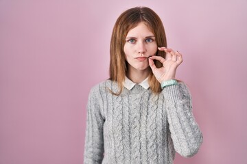 Beautiful woman standing over pink background mouth and lips shut as zip with fingers. secret and silent, taboo talking