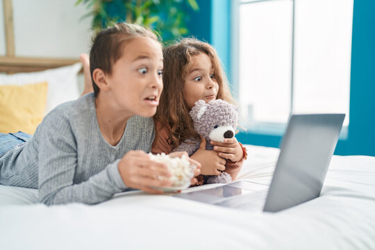Two kids watching movie on laptop lying on bed with scary expression at bedroom