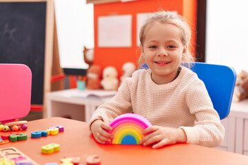 Adorable blonde girl playing with toys sitting on table at kindergarten