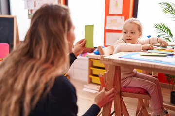 Teacher and toddler sitting on table having lesson at kindergarten