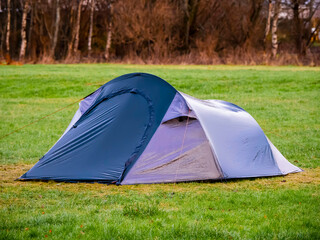 Blue tent on a green grass in a field forest in the background. Travel and tourism concept. Nobody. Active outdoor activity