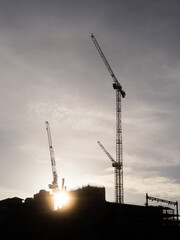 Silhouette of tall construction cranes at sunset. Dark moody sky. Construction industry. Building new commercial office of residence property.