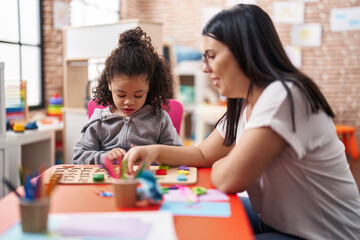 Teacher and toddler playing with maths puzzle game sitting on table at kindergarten