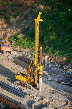 The yellow pile driver drives the foundation piles at the construction site.