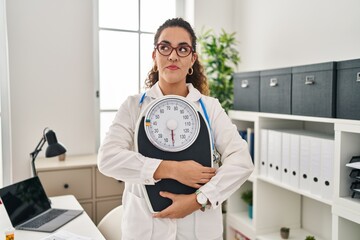 Young hispanic woman working at dietitian clinic smiling looking to the side and staring away...